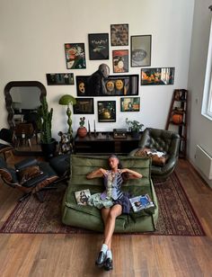 a woman sitting on top of a green couch in front of a wall filled with pictures