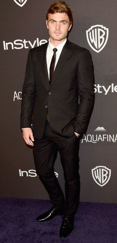 a man in a suit and tie standing on a purple carpet at an instyle event