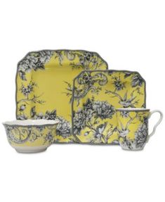 a yellow and black dinnerware set with flowers on the front, two cups and one saucer