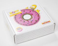 a pink donut with sprinkles sits in a box on a white surface