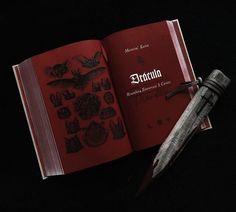 an open red book sitting on top of a black table next to a knife and a pen