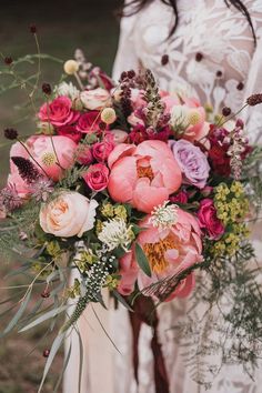 a bride holding a bouquet of pink and purple flowers with greenery on the side