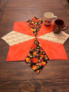 a coffee cup sits on top of an orange and black quilted table runner with autumn leaves