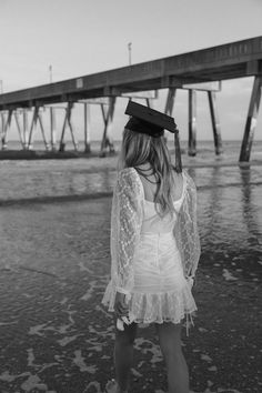 a woman in a graduation cap and gown standing on the beach with her back to the camera