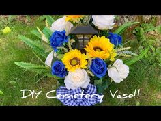 a wreath with sunflowers, roses and blue ribbon on the grass in front of a tree