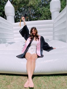 a woman sitting on top of an inflatable bed with her graduation cap and gown