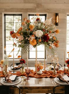 the table is set with orange and white flowers, gold candlesticks, and napkins