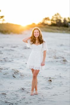 a woman standing in the sand with her hands behind her head and smiling at the camera