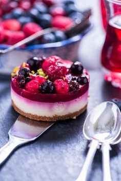 a cheesecake with berries and blueberries is on the table next to silverware