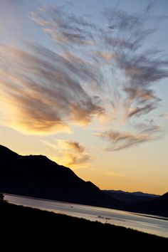 the sky is filled with clouds as the sun goes down over mountains and lake in the foreground