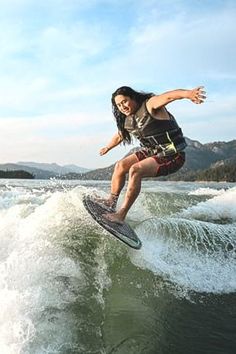 a woman riding a surfboard on top of a wave in the ocean with mountains in the background