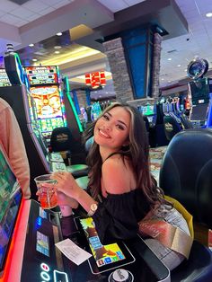 a woman sitting at a table with a drink in her hand and some slot machines behind her