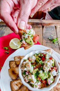 a person is dipping some food into a white bowl on top of tortilla chips