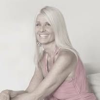 a woman sitting on top of a bed in a pink shirt and white pants with her legs crossed