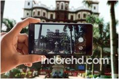 someone holding up their cell phone to take a photo in front of a building with palm trees