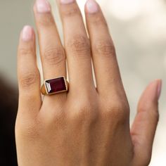 a woman's hand wearing a gold ring with a red stone in the middle