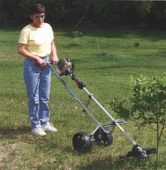 a woman is standing in the grass with a lawn mower on it's side