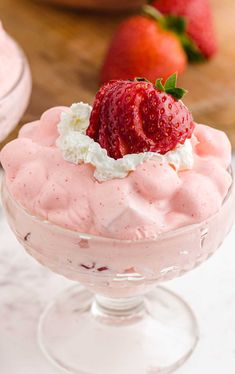 a dessert in a glass bowl with strawberries on the top and whipped cream around it