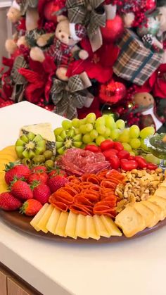 a platter filled with fruit and cheese next to a christmas tree