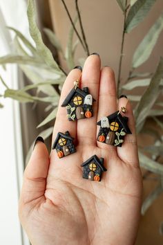 three miniature halloween houses in the palm of someone's hand with a plant behind them