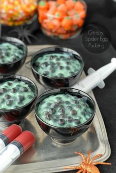 three glasses filled with green spider egg pudding on top of a tray next to halloween candies