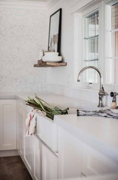 a kitchen with white cabinets and marble counter tops is pictured in this image, there are flowers on the window sill next to the sink