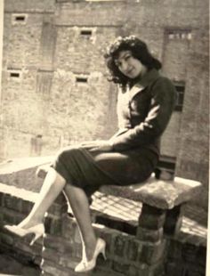 a woman sitting on top of a wooden bench next to a brick wall and building