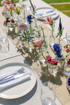 the table is set with flowers in glass vases and place settings for dinner guests