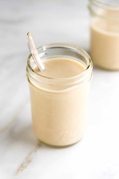 two jars filled with cream sitting on top of a white marble counter next to each other