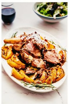 a white plate topped with meat and potatoes next to a bowl of salad on a table