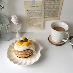 a white plate topped with pancakes covered in fruit next to a cup of coffee and an open book