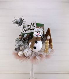 a snowman is sitting on top of a glass vase with christmas decorations around it