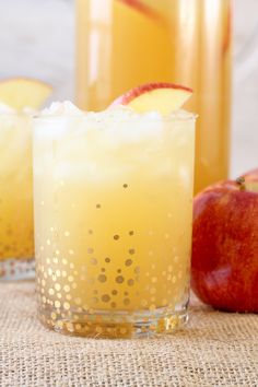 two glasses filled with apple cider on top of a table next to an apple