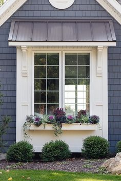 a house with two windows and plants in the window sill on the front porch