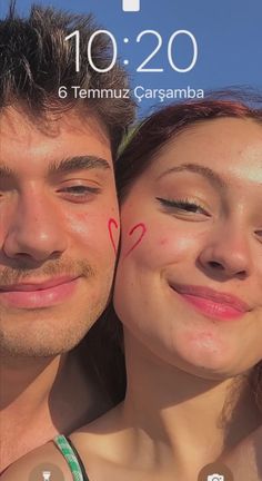 a man and woman smiling at the camera with hearts drawn on their foreheads in front of them