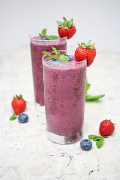 two glasses filled with blueberry smoothie next to strawberries and mint on the table