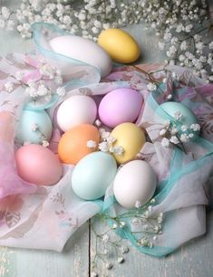 an arrangement of painted eggs on a white tablecloth with flowers in the background and baby's breath