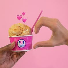 two hands holding up a pink cup with ice cream in it and hearts floating out