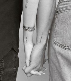 two people holding hands with tattoos on their arms