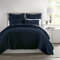 a bed with blue comforter and pillows in a white room next to a window