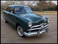 an old green car parked in a parking lot