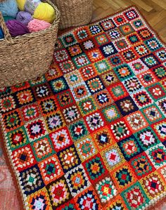 a crocheted granny's square rug next to a basket full of balls of yarn