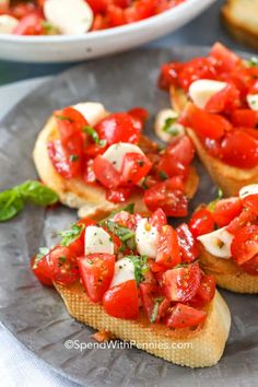 several pieces of bread topped with tomatoes and mozzarella on a plate next to a bowl of basil