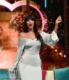 a woman in a gray dress on stage with her hand up to the side and mouth open