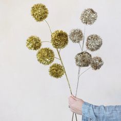 a person is holding some flowers in front of a white wall with gold florets on it