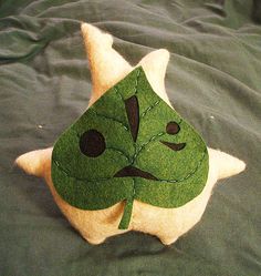 a close up of a pillow on a bed with a green face and leaf design