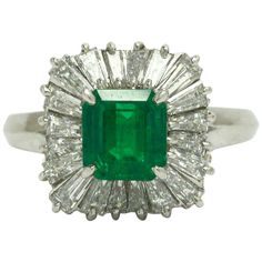 Centered by a breathtakingly lush and vivid green 1 1/2 carat emerald with a ballerina setting surrounded by 20 scintillating baguette diamonds. Named for the undulations of a tutu, the wavy design accentuates the gemstone and envelopes it with an outstanding, fiery brilliance. An original 1960 mid century platinum design, this classic, estate jewelry heirloom makes a statement without being over the top.   Condition: Very good Era: Mid century Year: 1960s Metal: Platinum Gemstone: Natural Emera