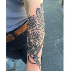 a person with a tattoo on their arm holding a scissors and flowers in the background