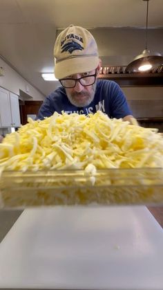 a man wearing a hat and glasses is looking at a large dish of food