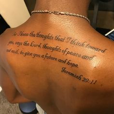 the back of a woman's neck with a bible verse tattooed on her lower back